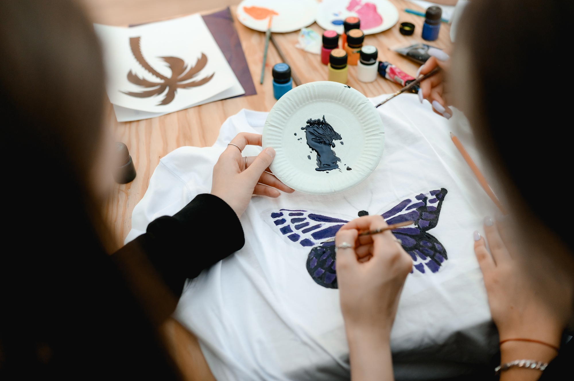 a woman sits at a table and paints a fashionable print on a white t-shirt